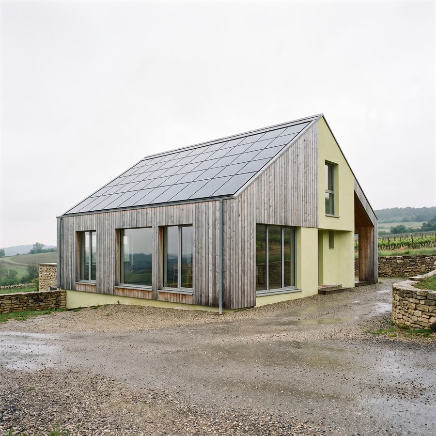 Maison passive bardée de mélèze grisé, panneaux intégrés affleurant le plan de toiture.